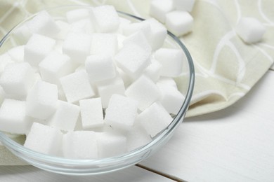 Photo of Many sugar cubes in glass bowl on white wooden table, closeup