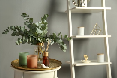Photo of Eucalyptus branches, aromatic reed air freshener and candles on table indoors, space for text. Interior element