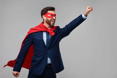 Photo of Happy businessman wearing red superhero cape and mask on beige background