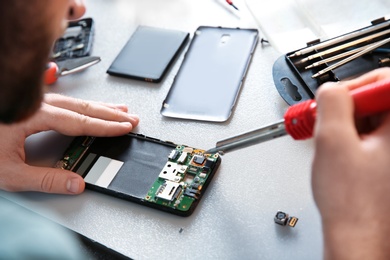 Photo of Technician repairing mobile phone at table, closeup