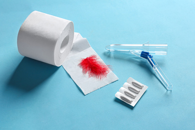 Photo of Anoscope, suppositories and toilet paper with red feather on light blue background. Hemorrhoid treatment