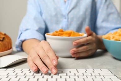Photo of Bad eating habits. Woman working on computer at light grey table with different snacks, closeup