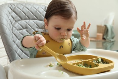 Photo of Cute little baby eating healthy food in high chair indoors