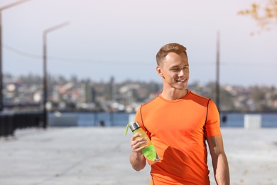 Photo of Young sporty man holding bottle of water outdoors on sunny day. Space for text