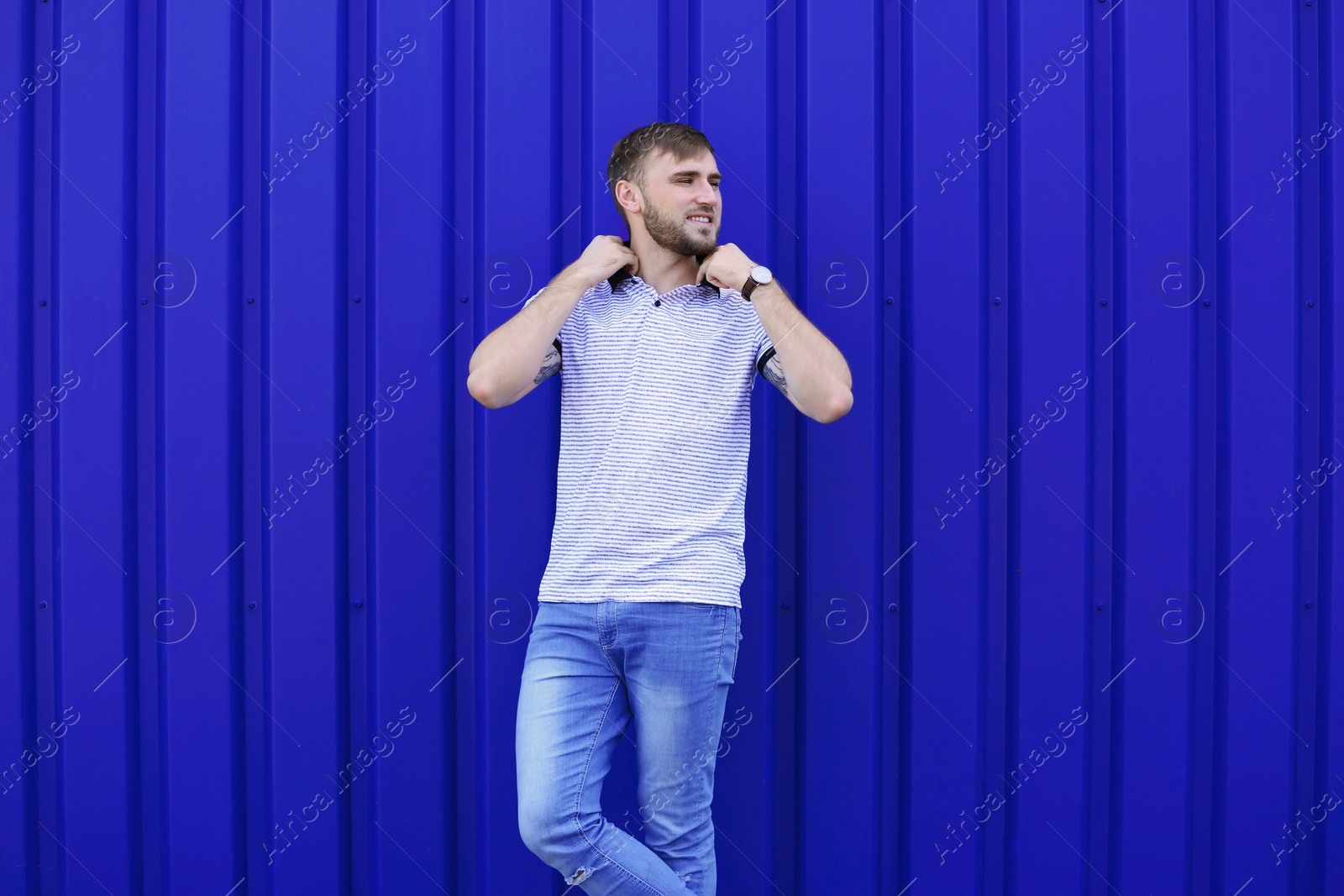 Photo of Young hipster man in stylish jeans posing near color wall