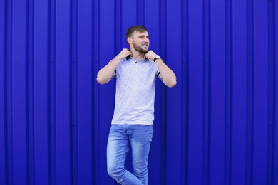 Photo of Young hipster man in stylish jeans posing near color wall