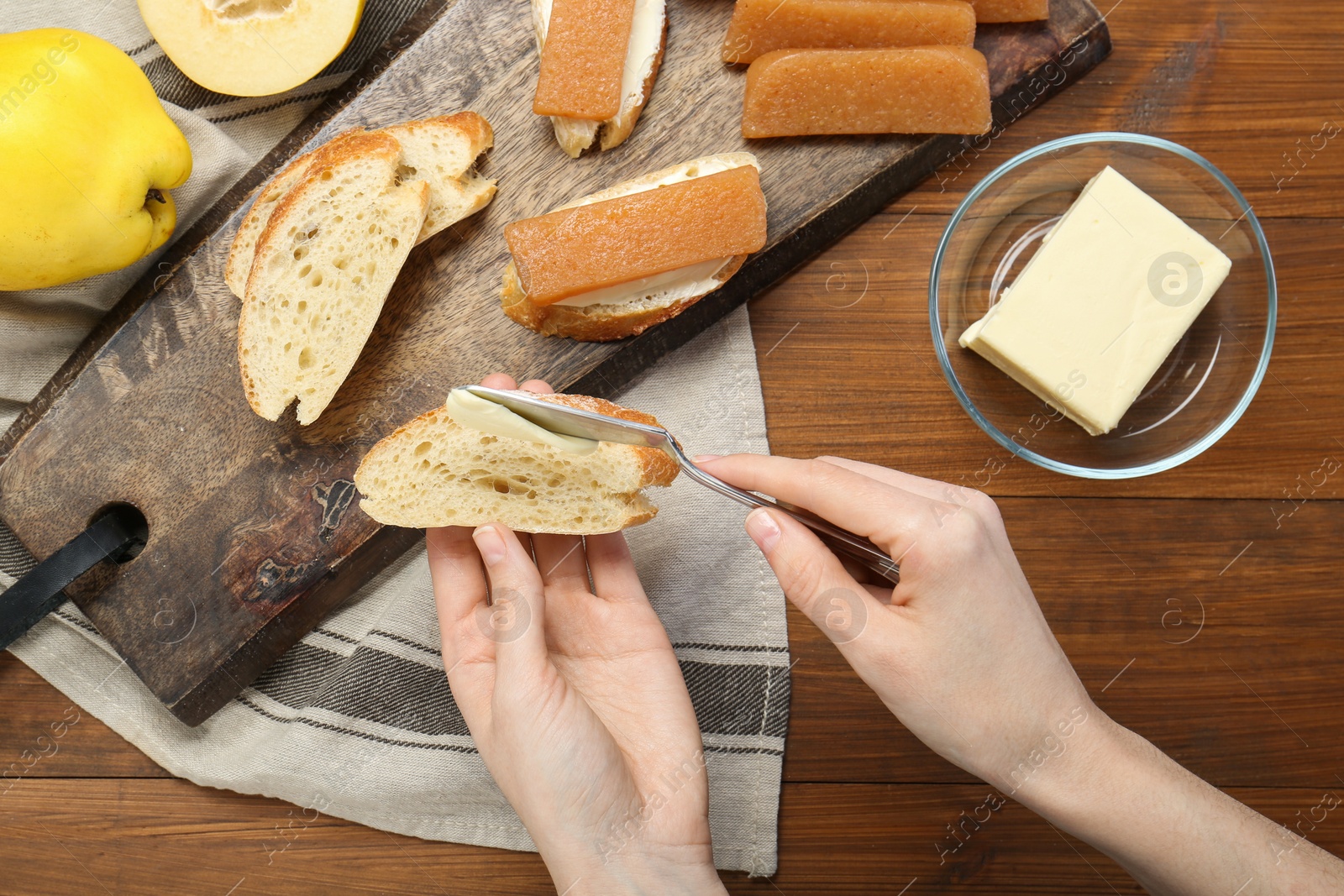 Photo of Making sandwich with quince paste. Woman buttering bread at wooden table, top view