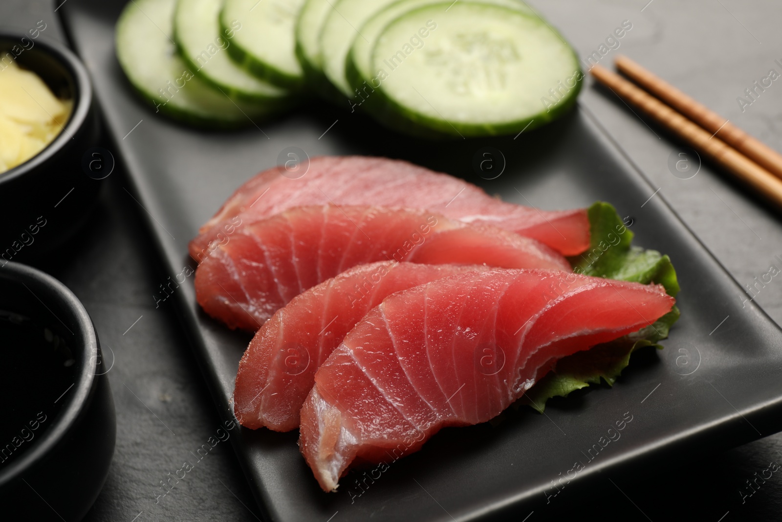 Photo of Tasty sashimi (pieces of fresh raw tuna) on black plate, closeup