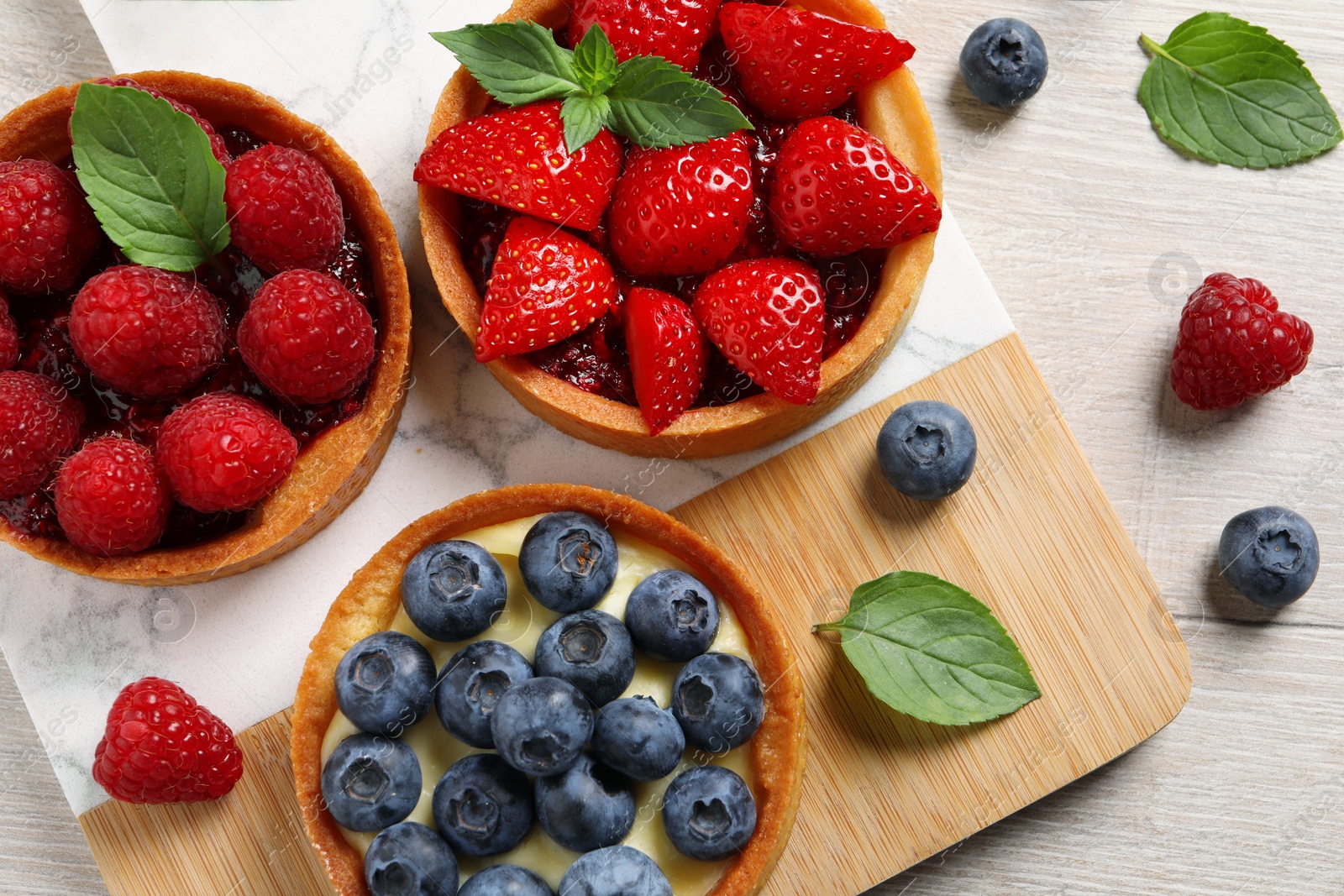 Photo of Tartlets with different fresh berries on light wooden table, flat lay. Delicious dessert