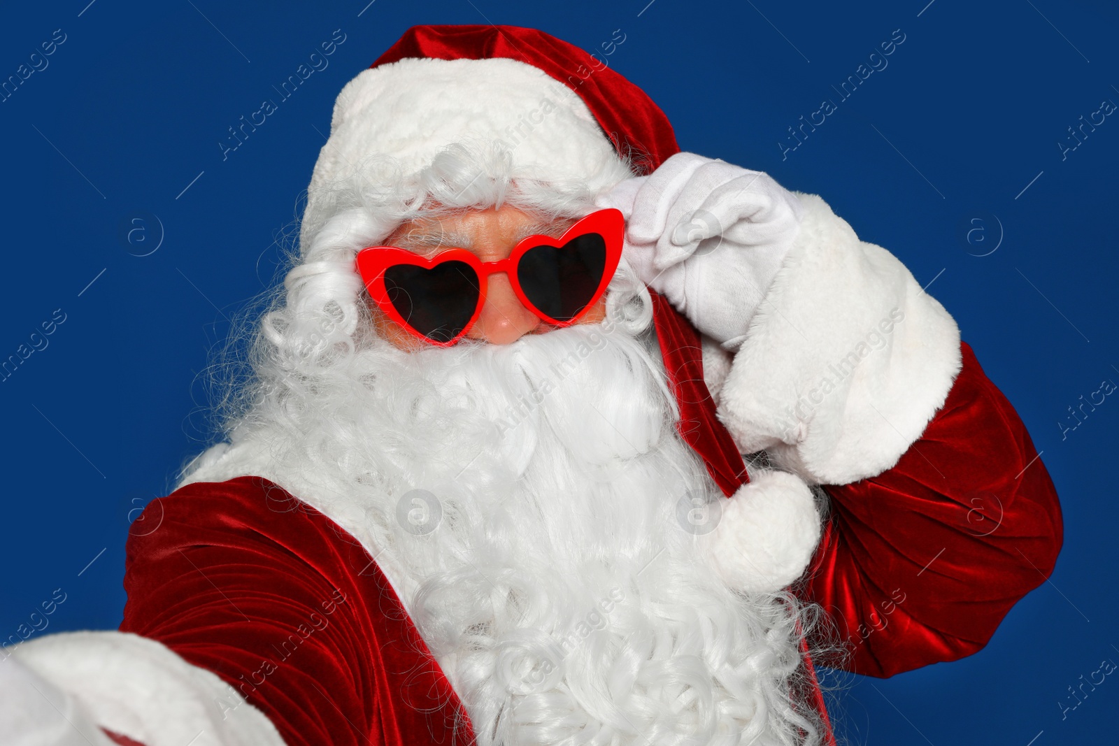 Photo of Authentic Santa Claus in sunglasses taking selfie on blue background