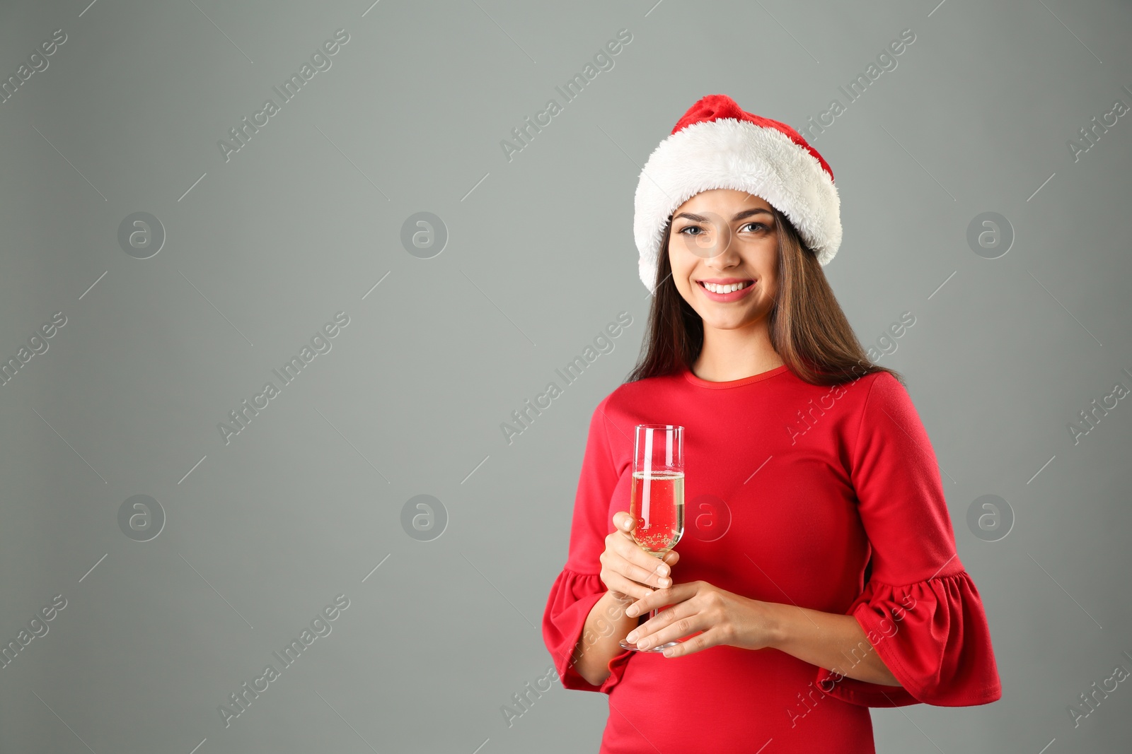 Photo of Young beautiful woman in Santa hat with glass of champagne on grey background. Christmas celebration