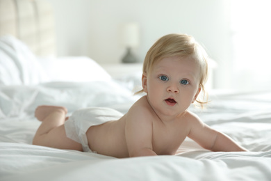 Photo of Cute little baby in diaper lying on bed at home