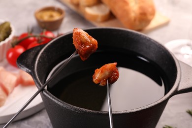 Fondue pot, forks with fried meat pieces and other products on grey table, closeup