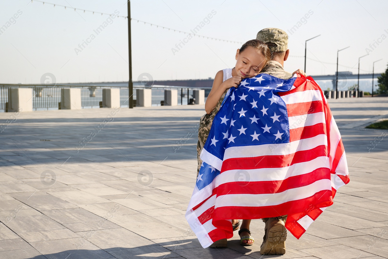 Photo of Soldier with flag of USA and his little daughter hugging outdoors, space for text