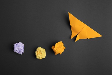 Photo of Handmade orange plane and crumpled pieces of paper on black background, flat lay. Startup concept