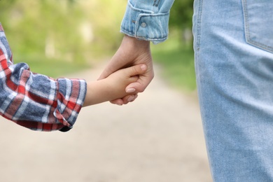 Little child holding hands with his mother outdoors, closeup. Family weekend