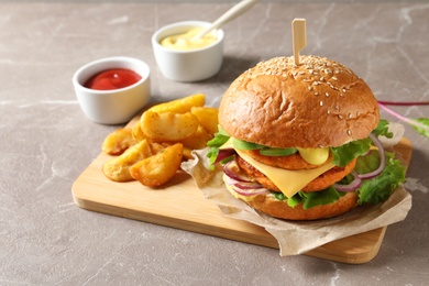Board with double vegetarian burger and fried potatoes on grey background