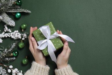 Christmas present. Woman with gift box, fir tree branches and festive decor on dark green background, top view. Space for text