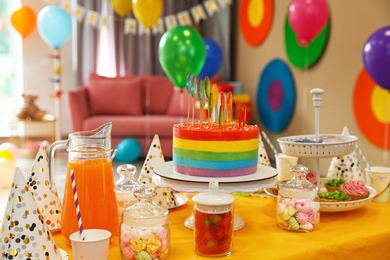 Photo of Bright birthday cake and other treats on table in decorated room