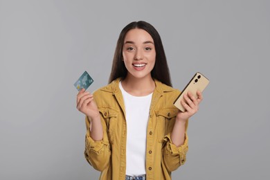 Photo of Happy woman with credit card and smartphone on light gray background. Debt free