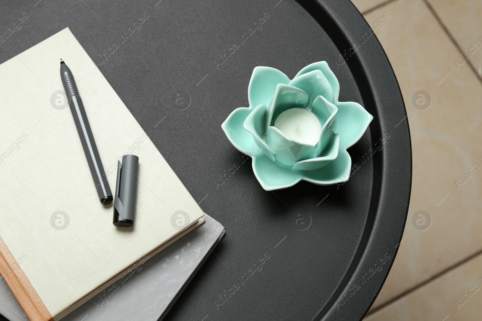 Photo of Notebooks, pen and candle in decorative holder on round table indoors, closeup