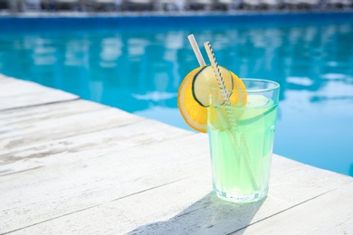 Photo of Refreshing cocktail near outdoor swimming pool on sunny day. Space for text