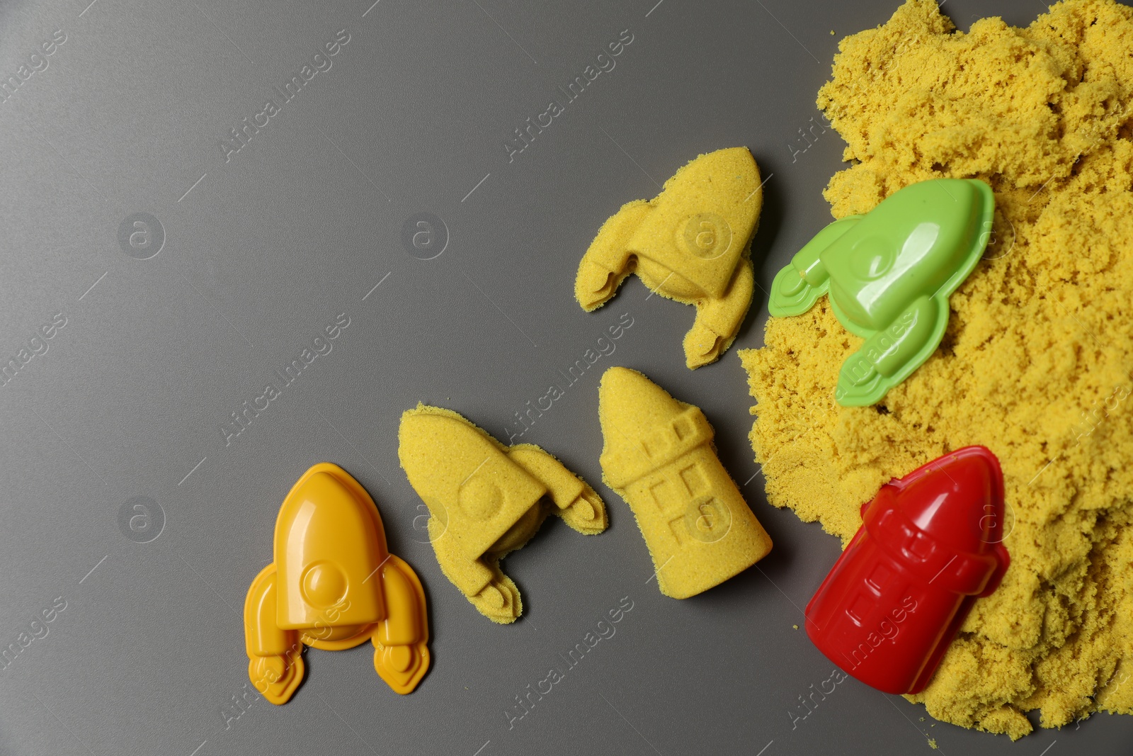 Photo of Different figures made of yellow kinetic sand and plastic toys on grey background, flat lay. Space for text