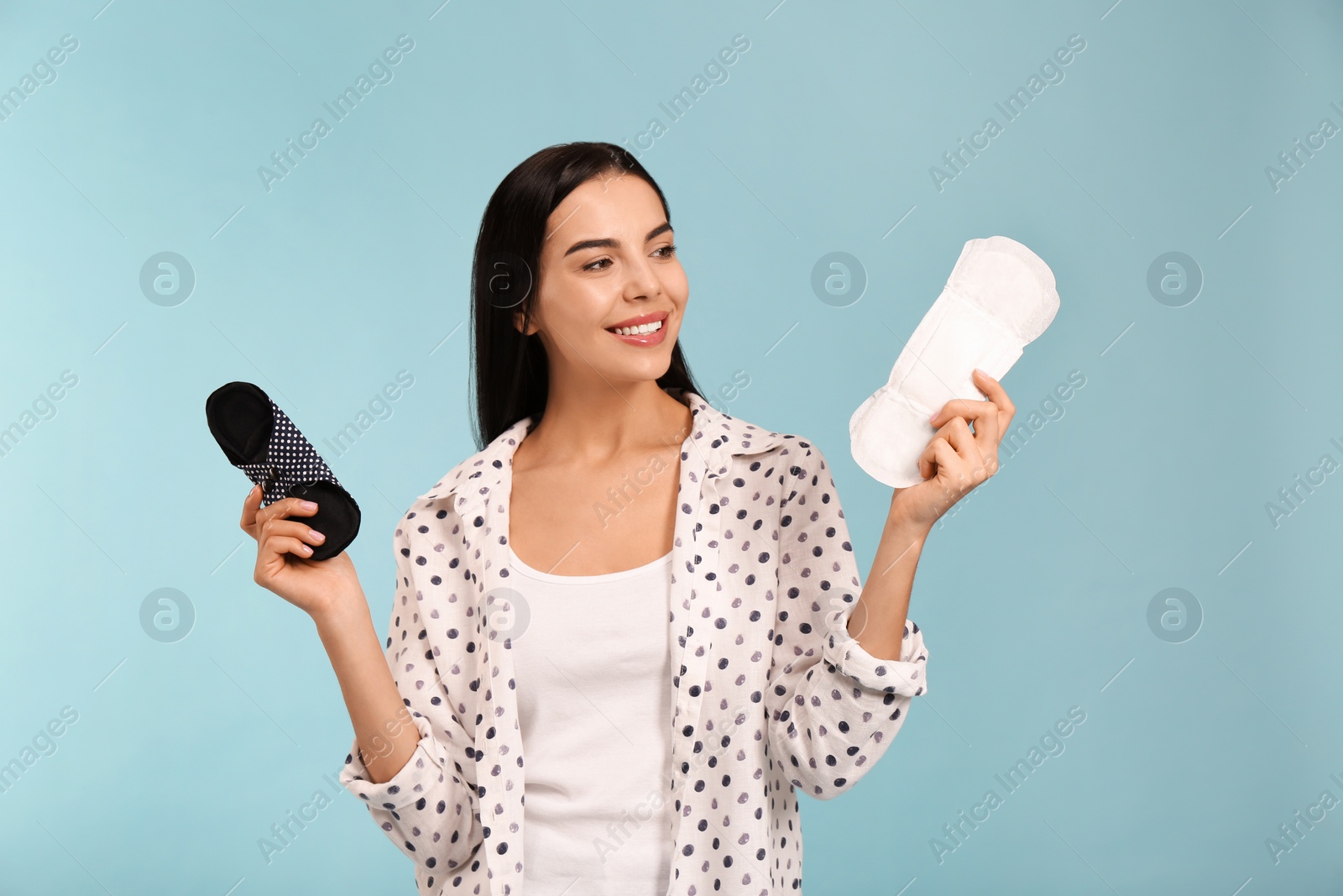 Photo of Young woman with reusable and disposable menstrual pads on light blue background