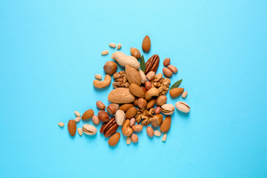 Different delicious nuts on light blue background, flat lay