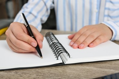 Woman writing in notebook at wooden table indoors, closeup