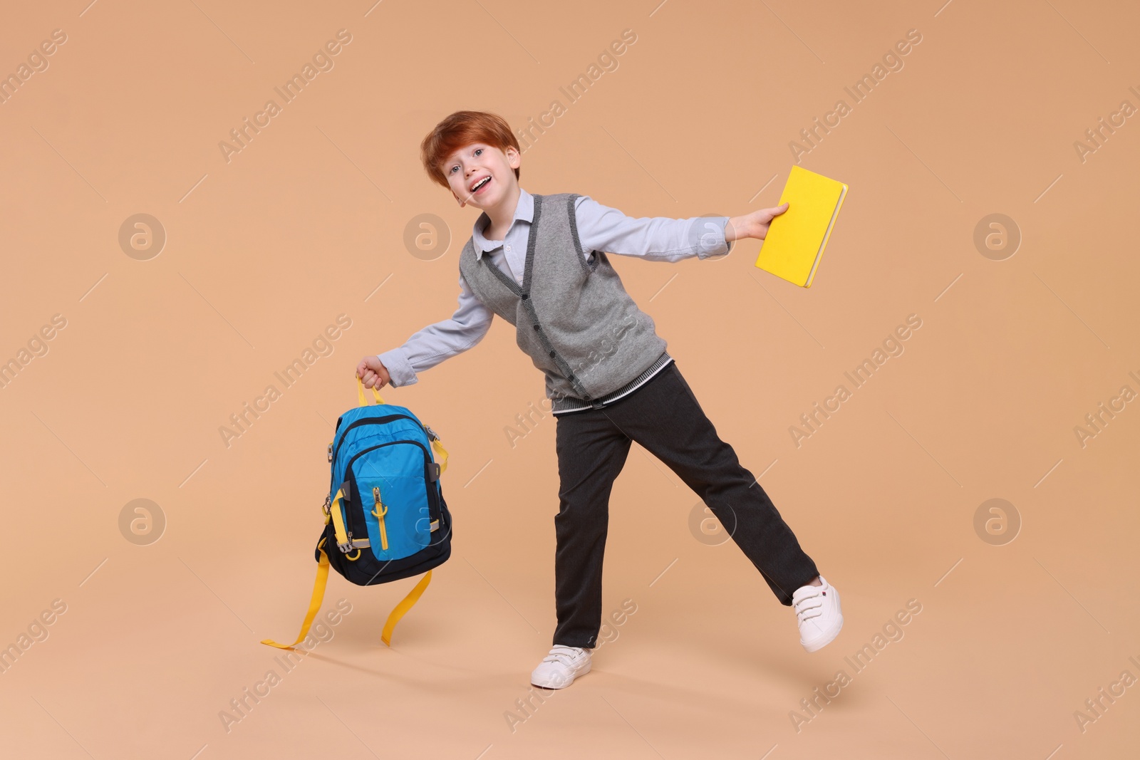 Photo of Happy schoolboy with book and backpack on beige background