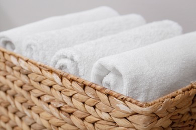 Photo of Set of clean white towels in wicker basket against grey background, closeup. Tidying up method