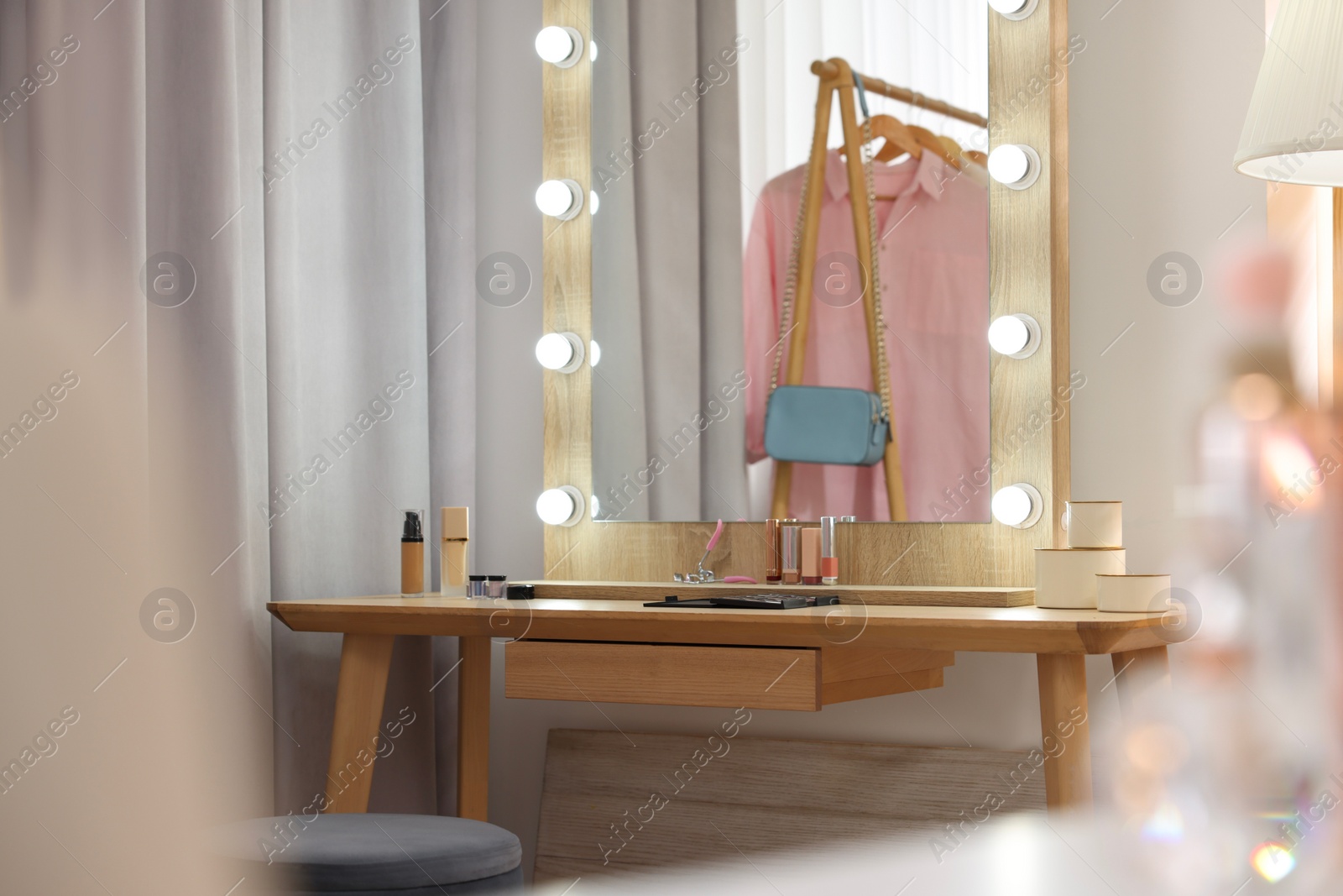 Photo of Stylish mirror with light bulbs and beauty products on wooden dressing table in makeup room