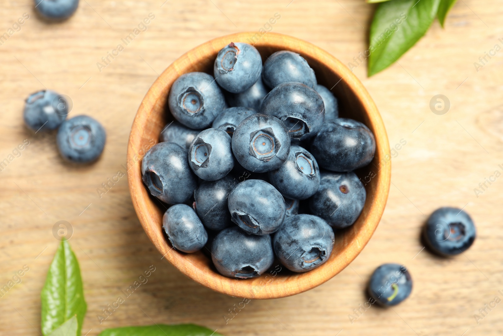 Photo of Bowl of fresh tasty blueberries on wooden table, flat lay