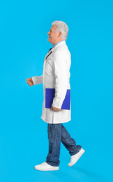 Photo of Senior doctor with clipboard walking on light blue background