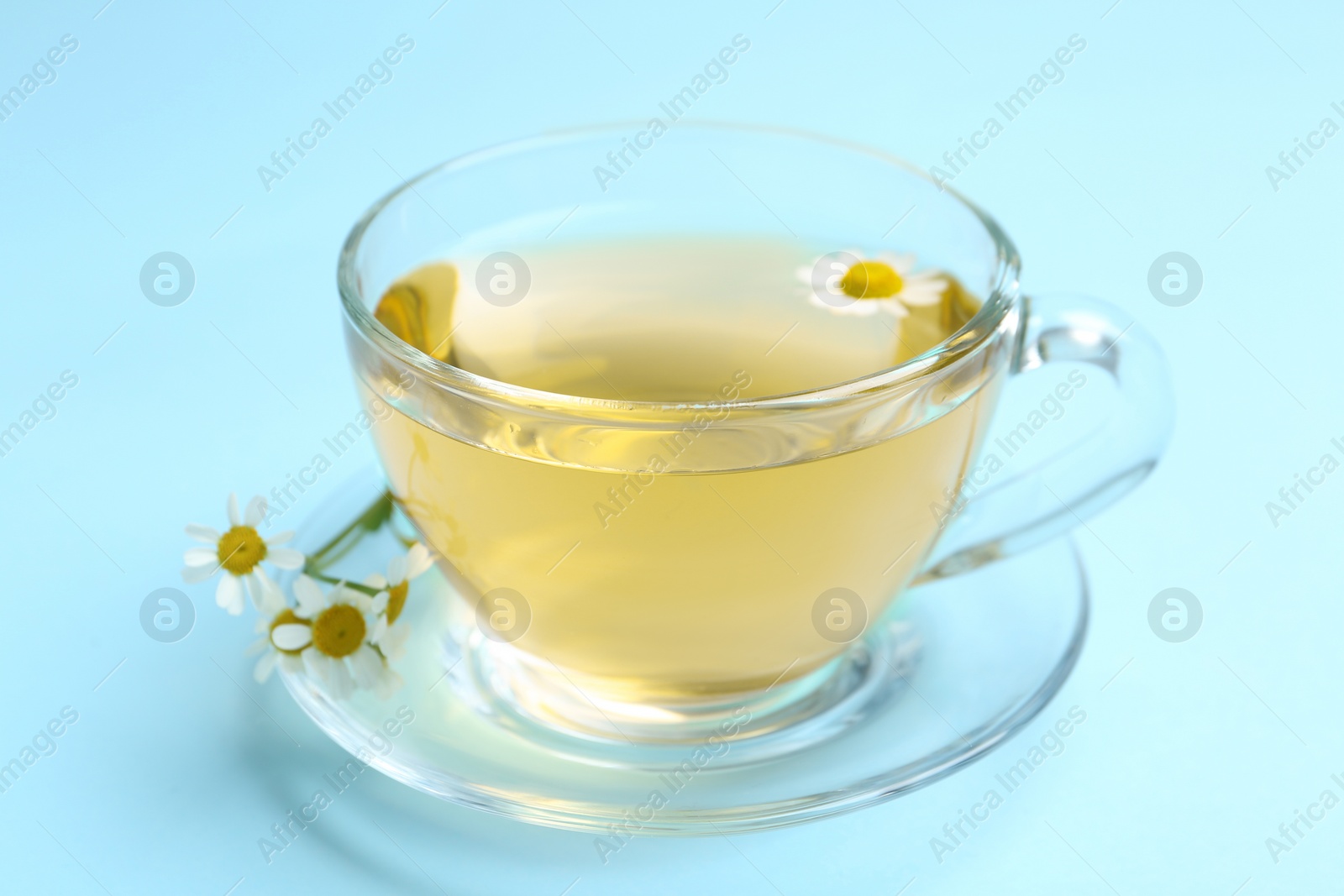 Photo of Delicious chamomile tea in glass cup on light blue background