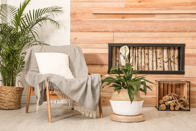 Beautiful plants and armchair near wooden wall. Stylish interior design