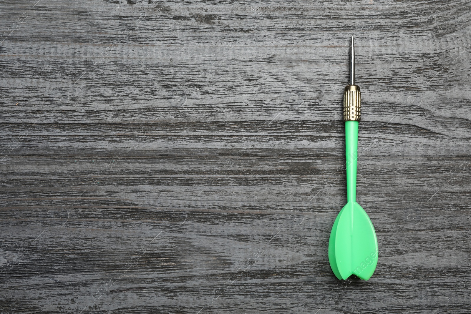 Photo of Green dart arrow on grey wooden table, top view with space for text