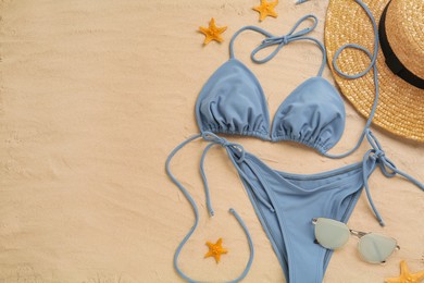 Stylish bikini, sunglasses, straw hat and starfishes on sand, flat lay. Space for text