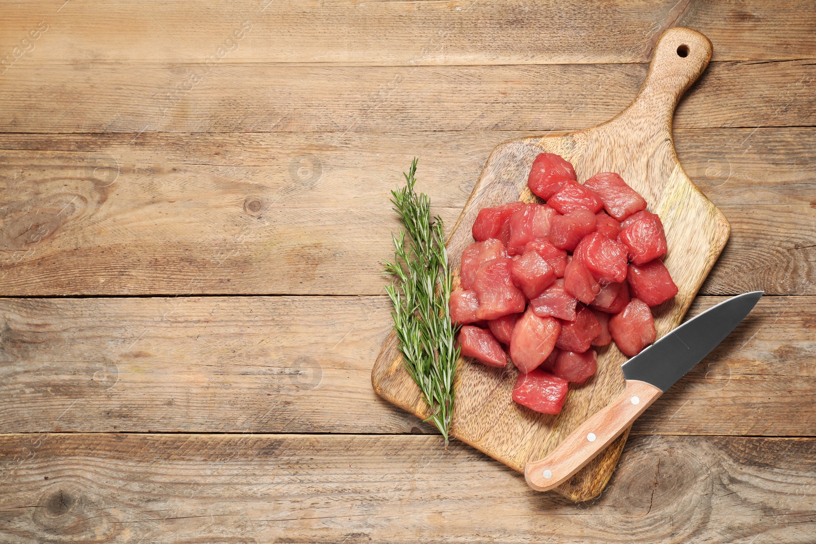 Photo of Cooking delicious goulash. Raw beef meat, rosemary and knife on wooden table, top view. Space for text