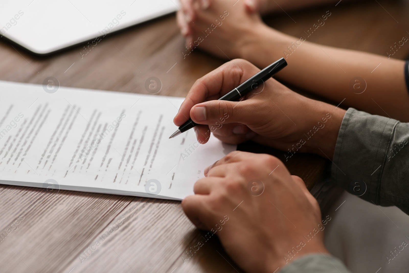 Photo of Notary helping couple with paperwork at wooden table, closeup