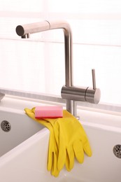 Photo of Sponge and rubber gloves on kitchen sink indoors