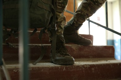 Military mission. Soldier in uniform on stairs inside abandoned building, closeup