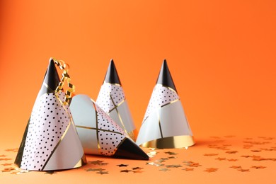 Party hats and confetti on orange background, space for text