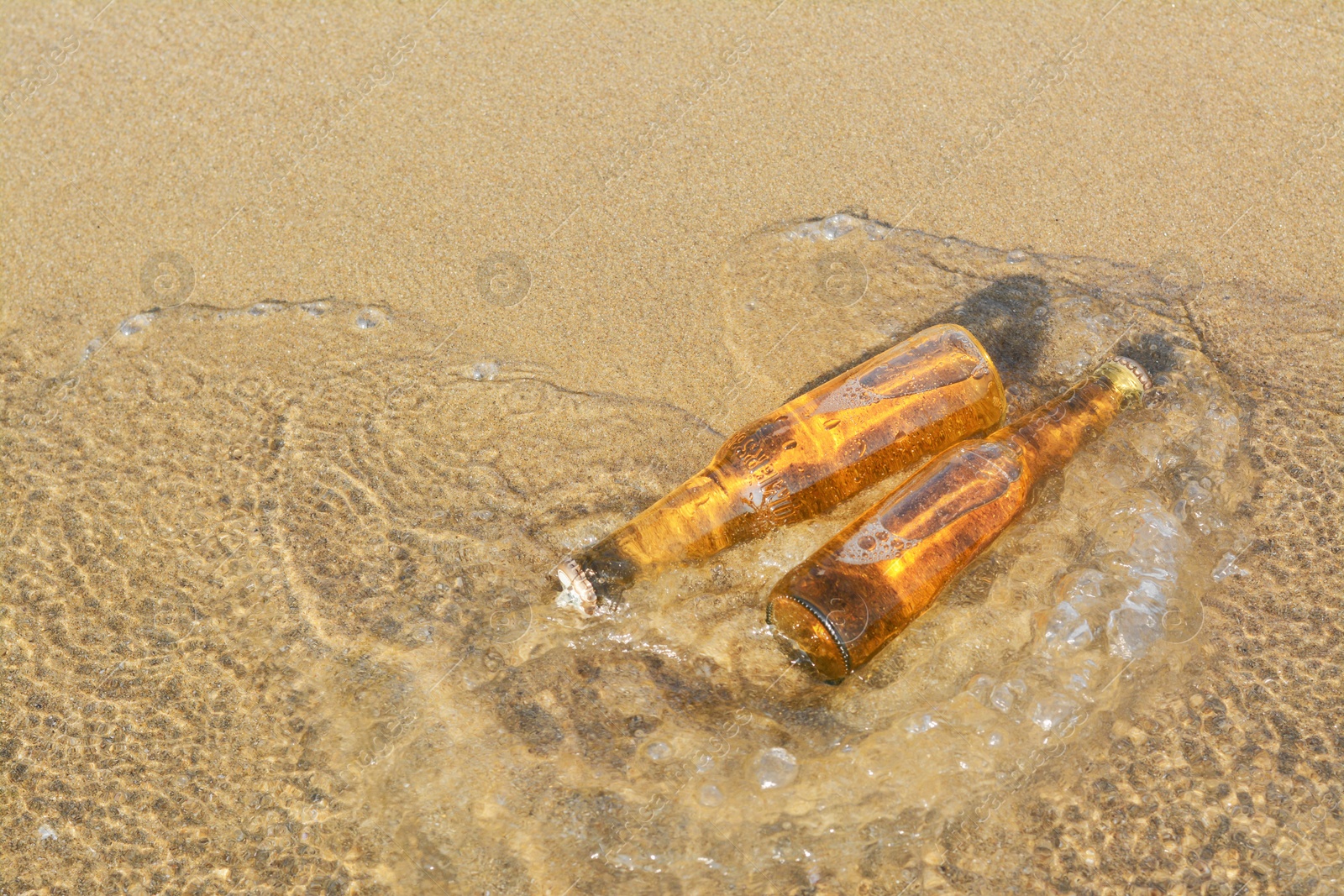 Photo of Bottles of cold beer on sandy beach near sea, space for text