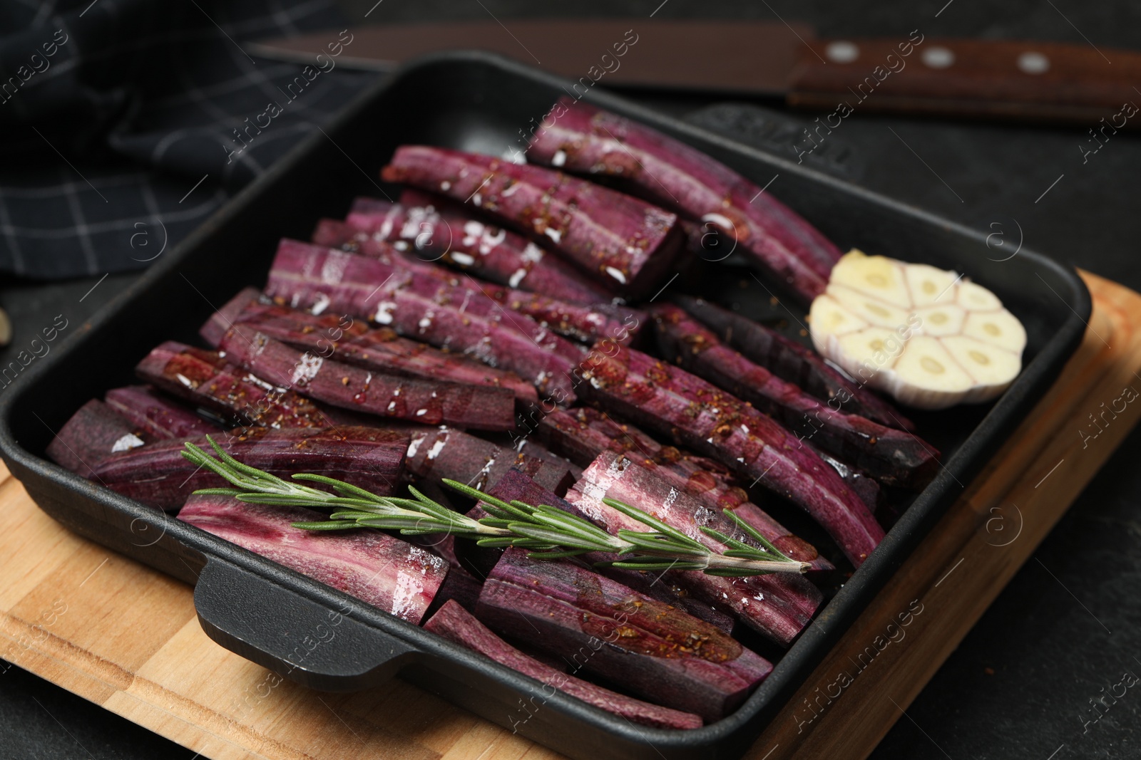 Photo of Black raw cut carrot with garlic and rosemary in baking dish on black table, closeup