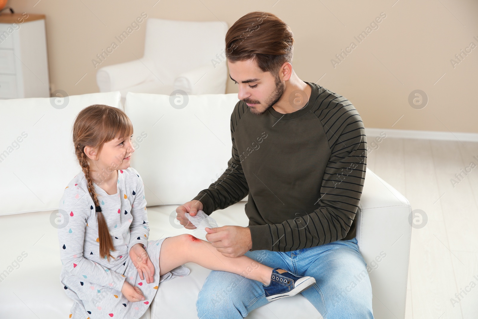 Photo of Father applying bandage on daughter's injured knee at home. First aid