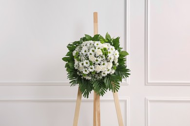 Photo of Funeral wreath of flowers on wooden stand near white wall