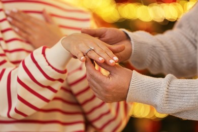 Photo of Making proposal. Man putting engagement ring on his girlfriend's finger against blurred lights, closeup