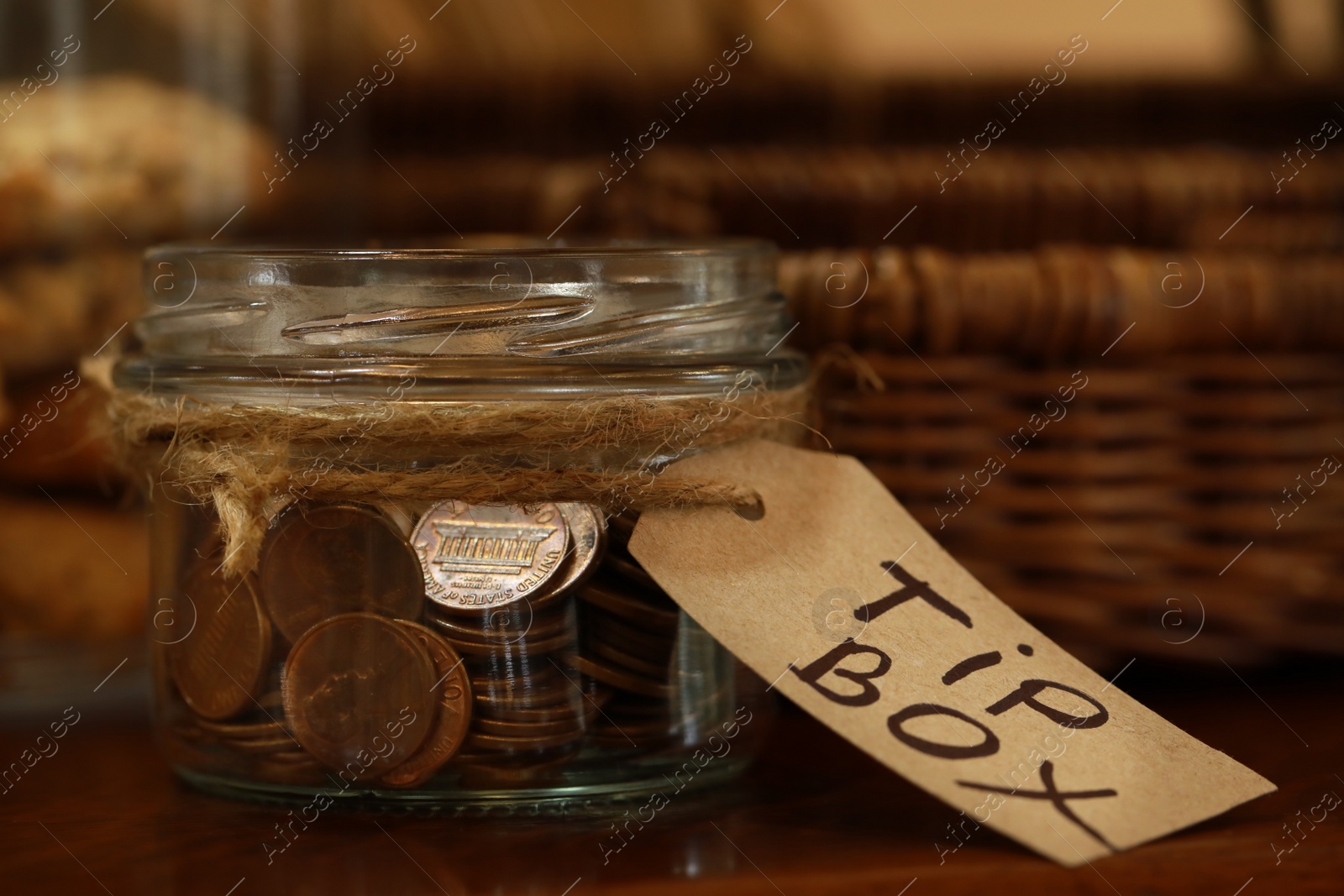 Photo of Tip box full of coins on wooden table in cafe, closeup